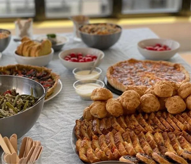 Table d'un cocktail dînatoire préparé par Les Régalades de Delphine. Sur la table : tartes salées, salades de pâtes et de haricots verts, crudités, gougères et tranches de cakes salés.