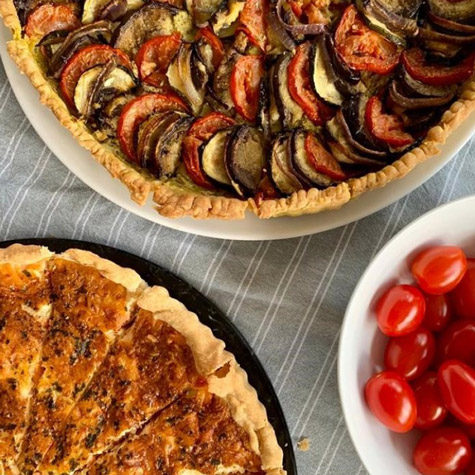 Vue de dessus d'un table de cocktail dînatoire préparé par Les Régalades de Delphine, traiteur paris 20. Sur la table : parts de quiche et de tarte salée aux légumes accompagnées de crudités.